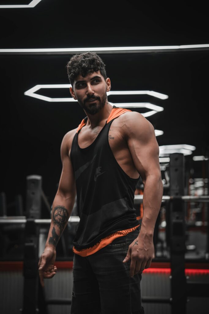 Fit man in gym showcasing muscles wearing black tank top. Modern interior.