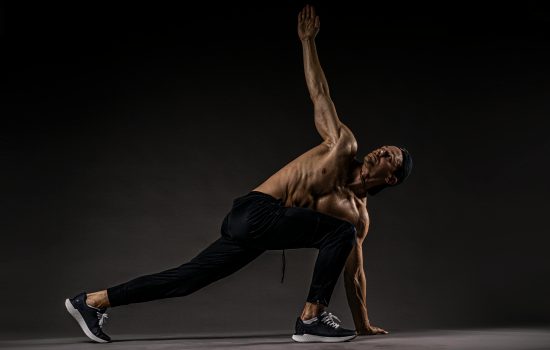 Shirtless man performing fitness stretch highlighting muscles and flexibility.