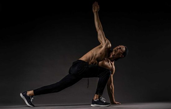 Shirtless man performing fitness stretch highlighting muscles and flexibility.