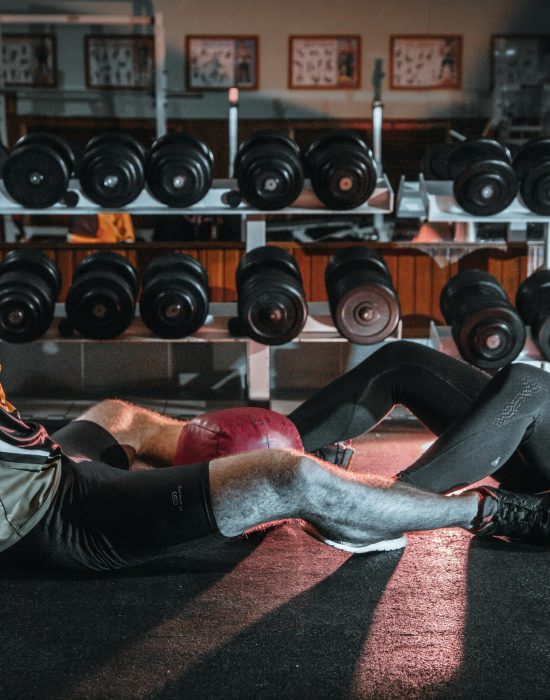 A man and woman resting together on the gym floor, surrounded by dumbbells.