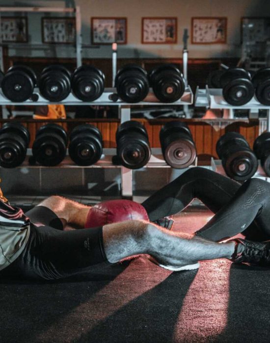 A man and woman resting together on the gym floor, surrounded by dumbbells.